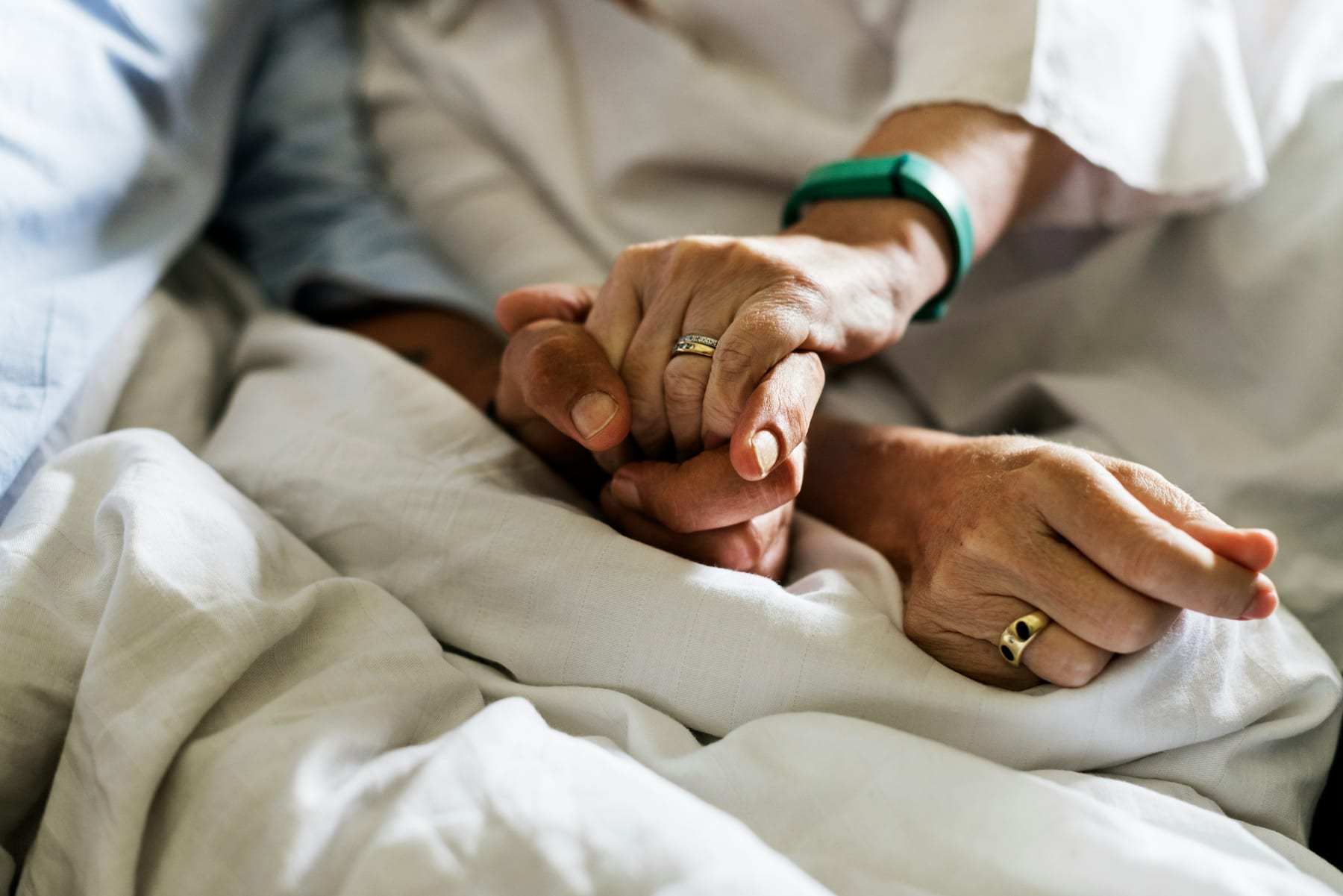 One person holding another person’s hand beside a bed